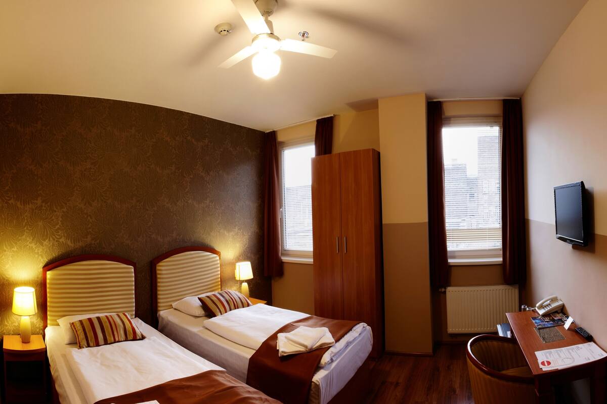 A hotel room with two beds, a desk with a telephone, and a TV on the wall.