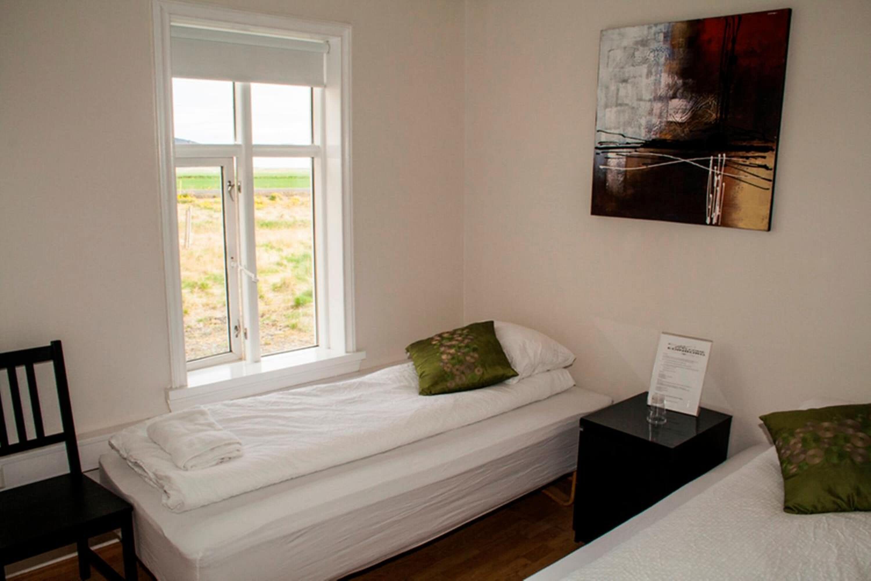 A single bed with white bedding, a green pillow, and a black nightstand with a glass and a sign.
