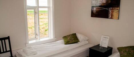 A single bed with white bedding, a green pillow, and a black nightstand with a glass and a sign.