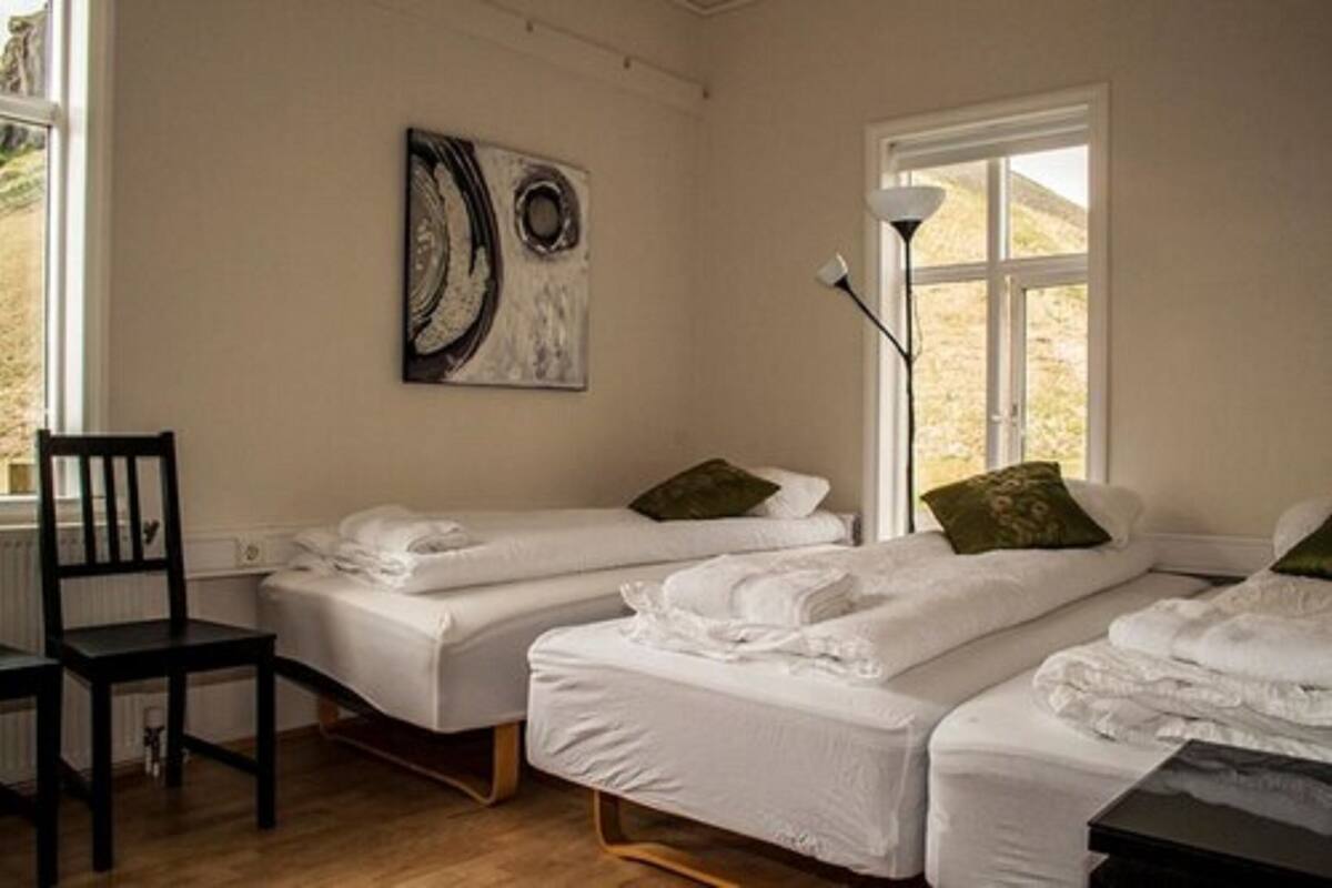 Una habitación con dos camas individuales, una silla, una lámpara y un cuadro en la pared.