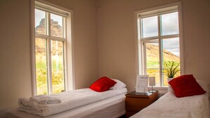 Habitación con dos camas, cada una con ropa blanca y almohadas rojas, y una mesita de noche con una lámpara.