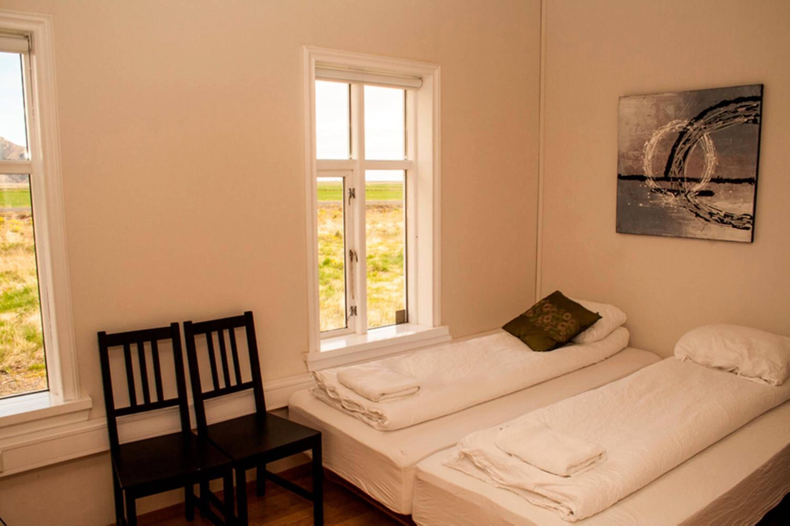 Una habitación con dos camas individuales, una silla y una ventana que da a un campo.