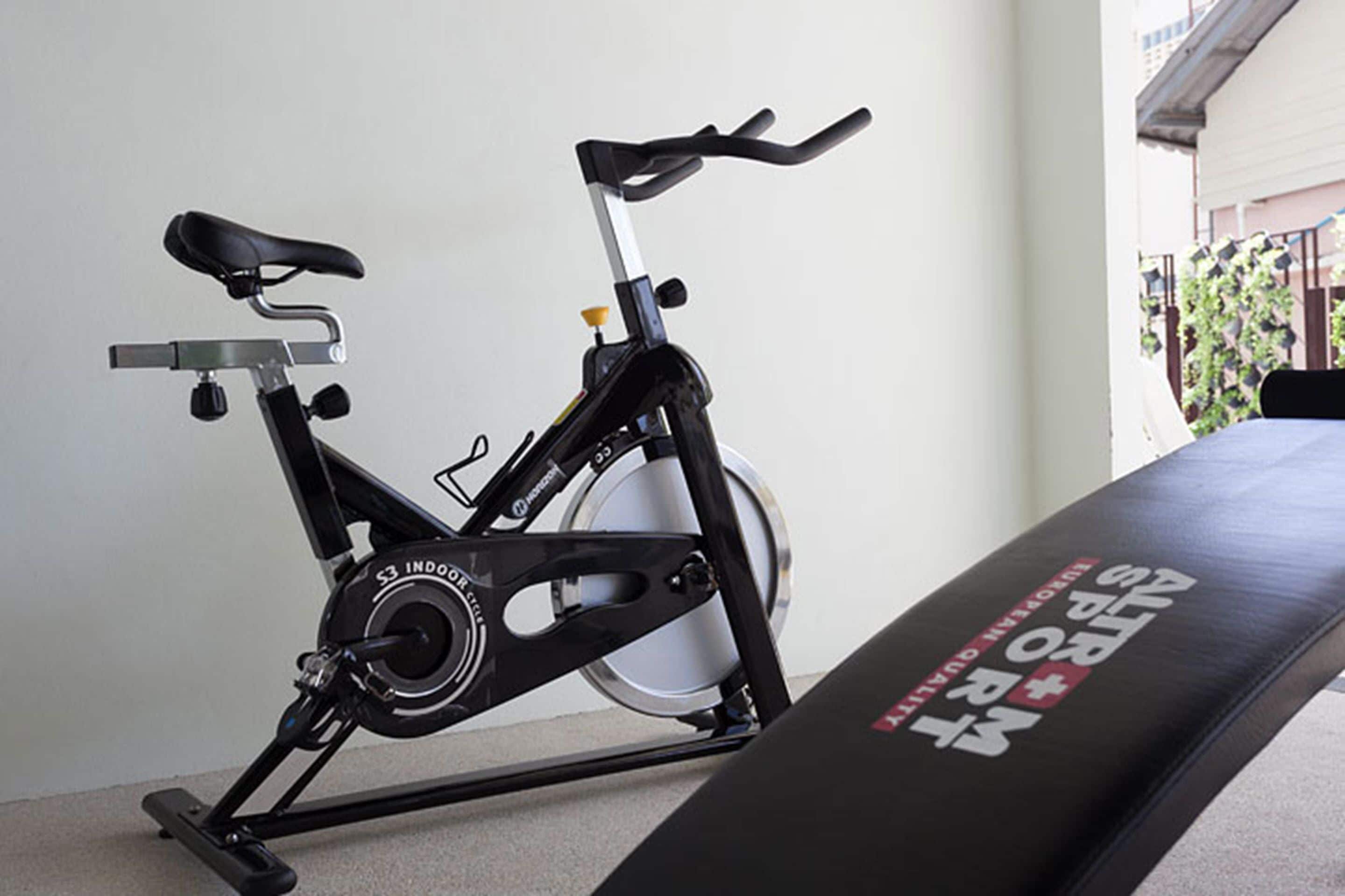 A stationary bike in a room with a black padded bench.