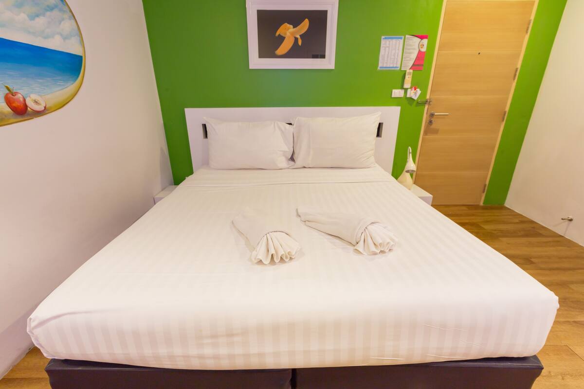 Ein ordentlich bezogenes Bett mit weißen Leinen und Kissen, ein gerahmtes Bild an der Wand und eine Holztür im Hintergrund.