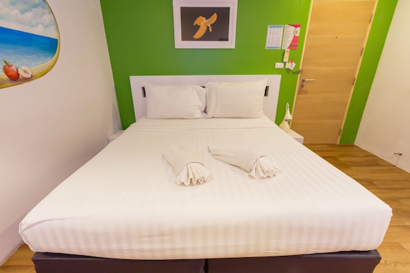A neatly made bed with white linens and pillows, a framed picture on the wall, and a wooden door in the background. - The Frutta Boutique Patong Beach (Patong)