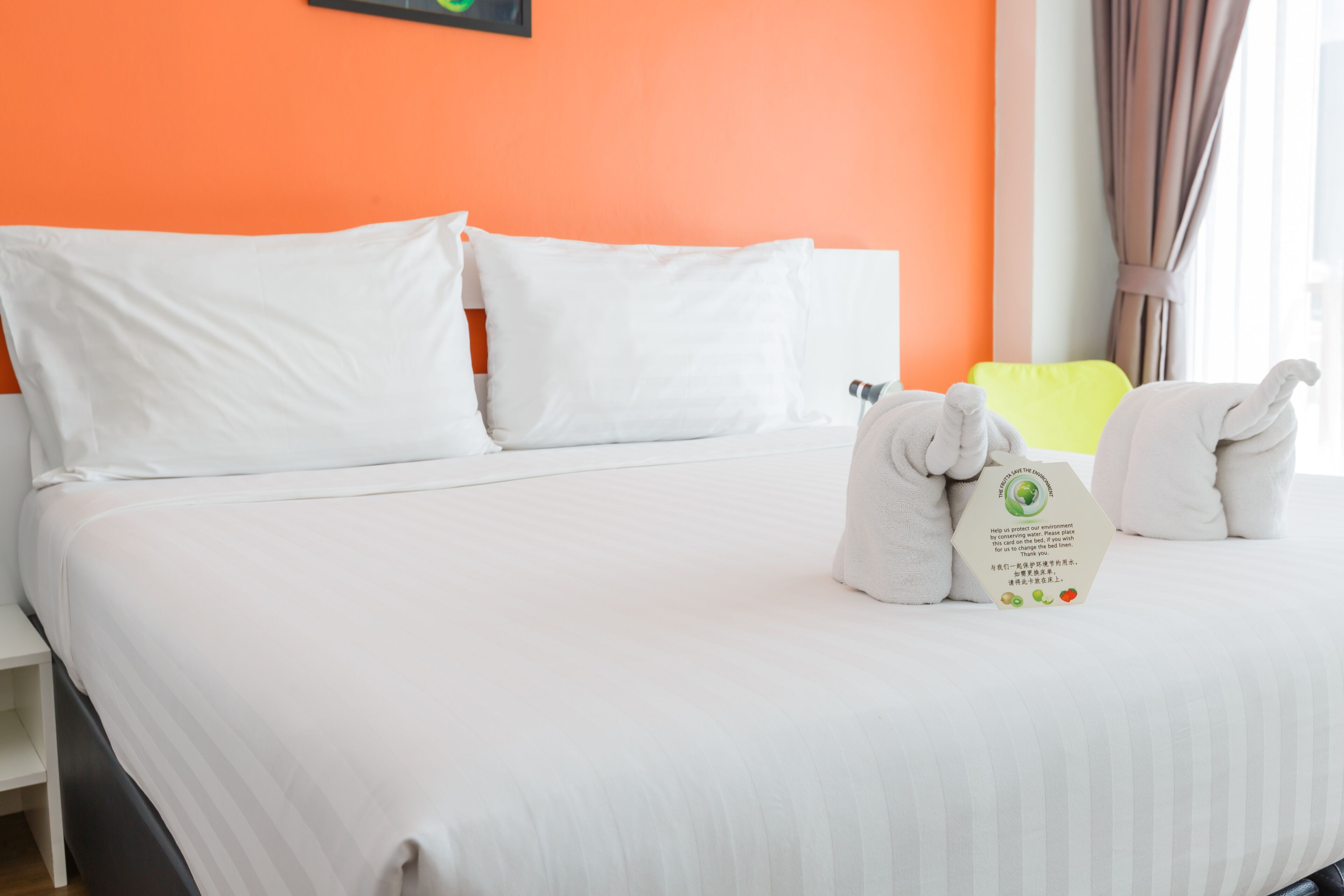 A neatly made bed with white linens, a pillow, and a set of towels on the side.