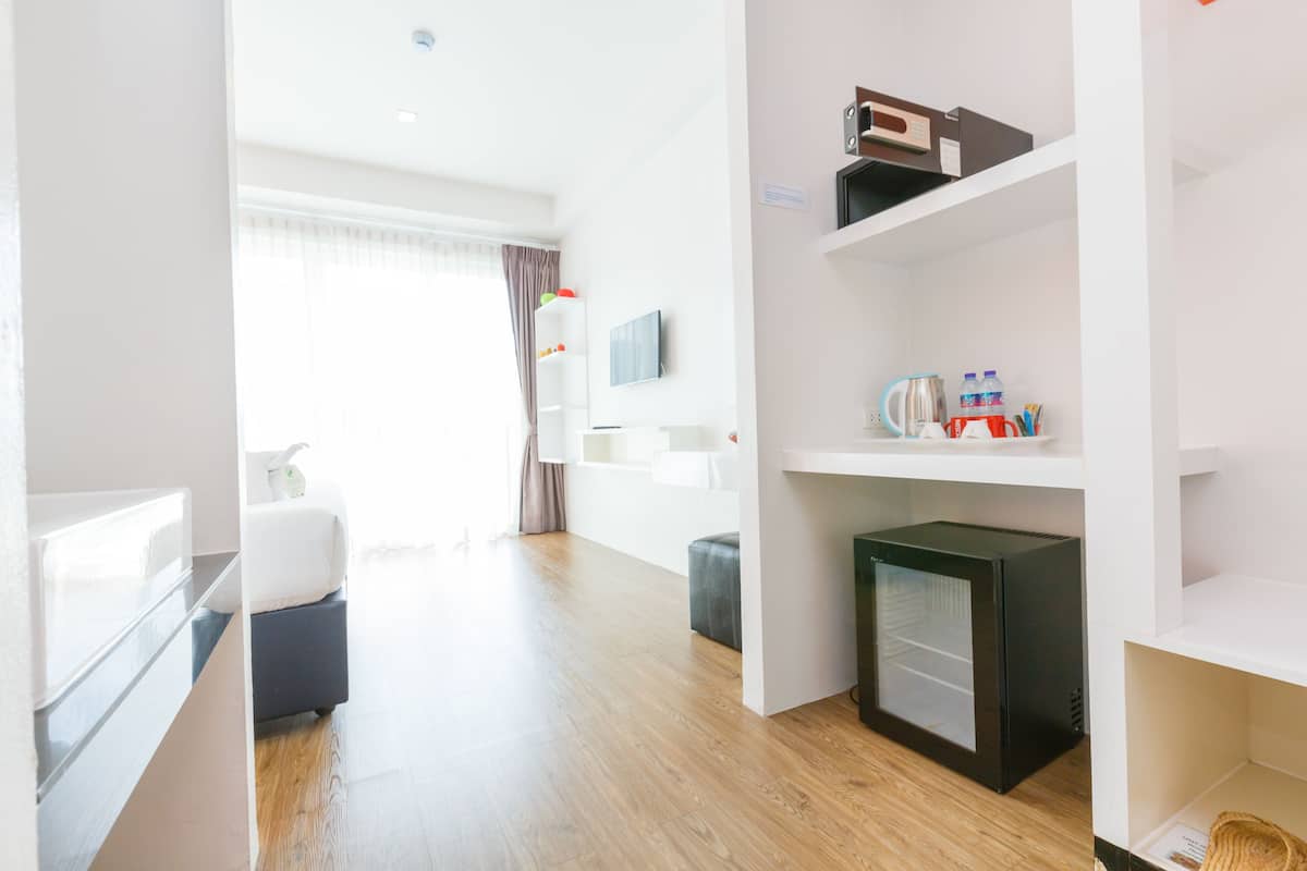 Ein modernes Hotelzimmer mit Holzboden, einem Bett, einer kleinen Küchenzeile und einem an der Wand montierten Fernseher.