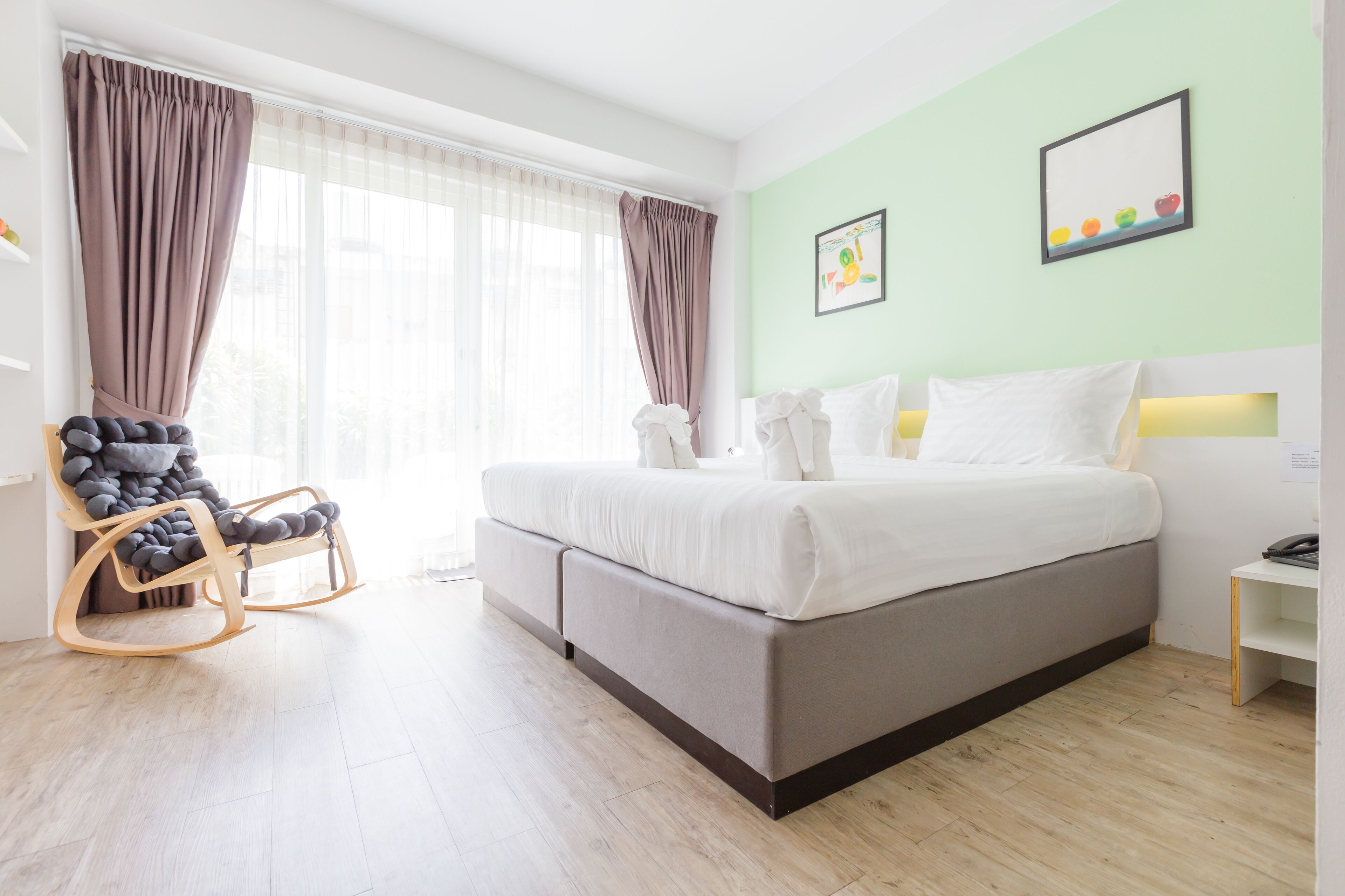A modern bedroom with a large bed, a rocking chair, and a window with sheer curtains.