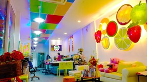 A brightly lit room with a colorful ceiling, a reception desk, a yellow sofa, and a wall decorated with fruit cutouts. - The Frutta Boutique Patong Beach (Patong)