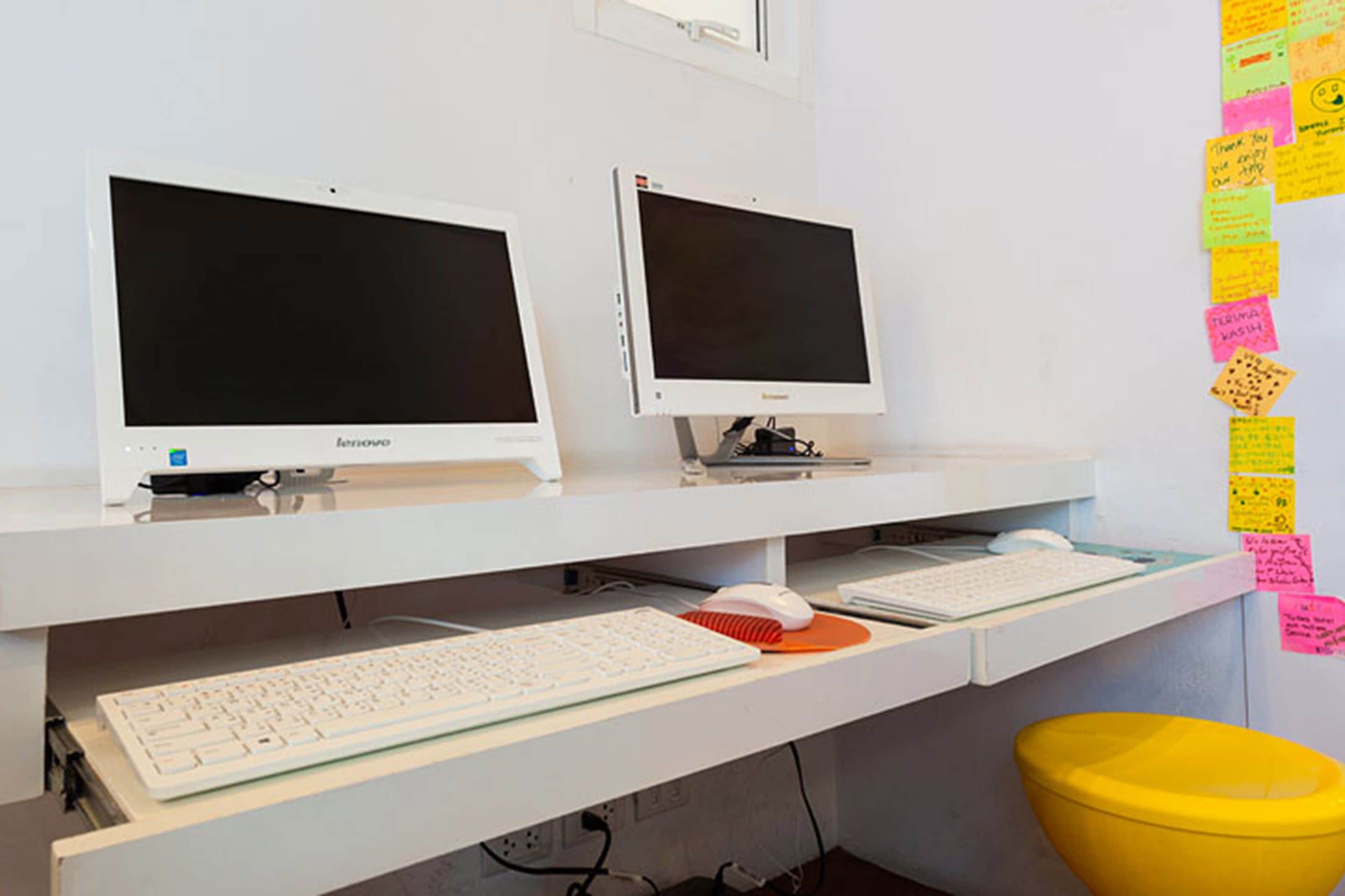 A workspace with two monitors, a keyboard, and a mouse on a white desk. There are sticky notes on the wall to the right.