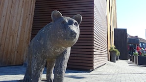 Una estatua de oso frente a un edificio con fachada de madera y estructura de concreto encima.