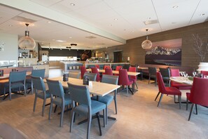 En moderne restaurant med blålige og røde stole, træborde og et stort maleri af et bjerg på væggen.