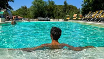 Un uomo in piscina, con acqua cristallina, circondato da sdraio e da un'area a bordo piscina.