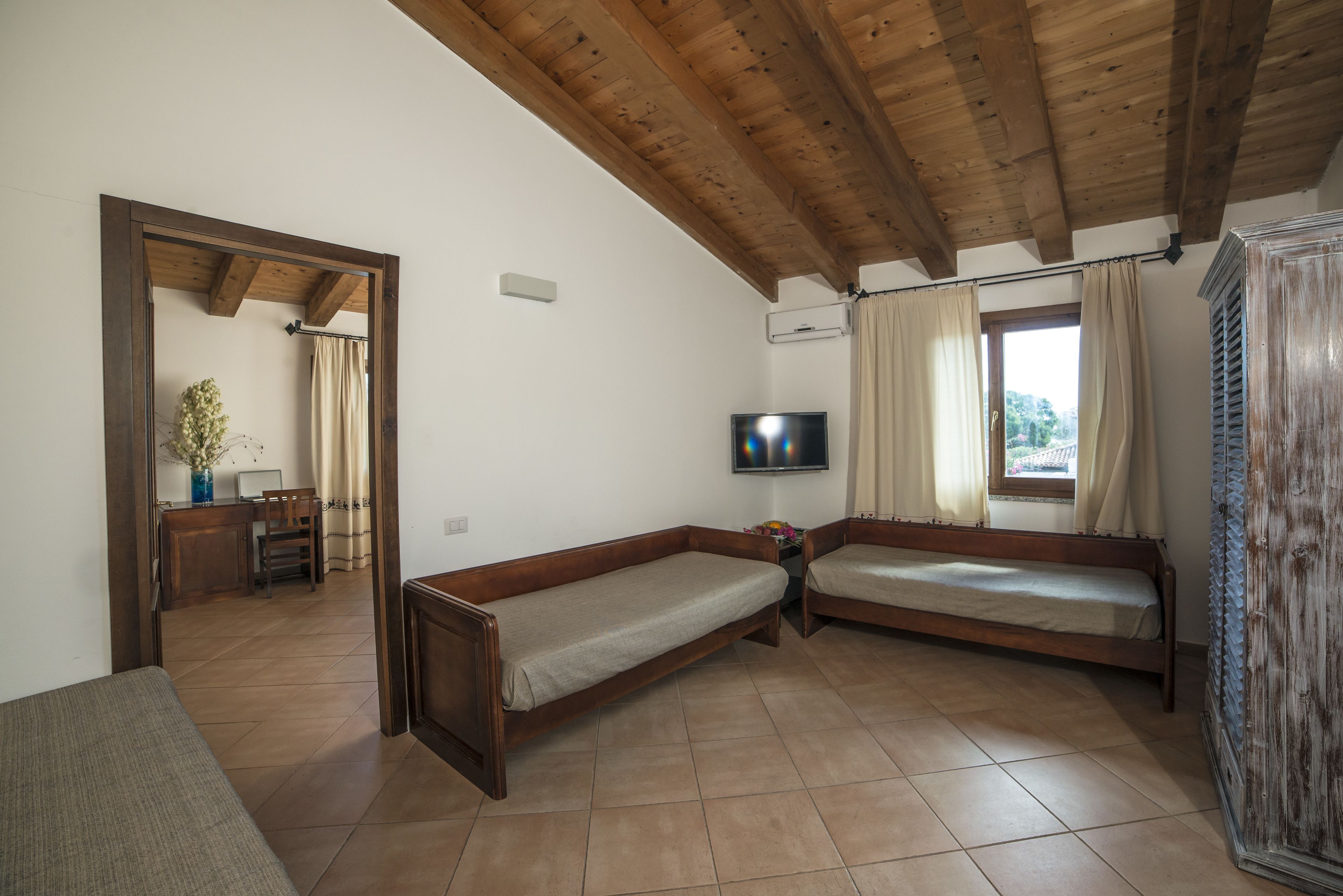 A room with two wooden beds, a TV, and a window with curtains.