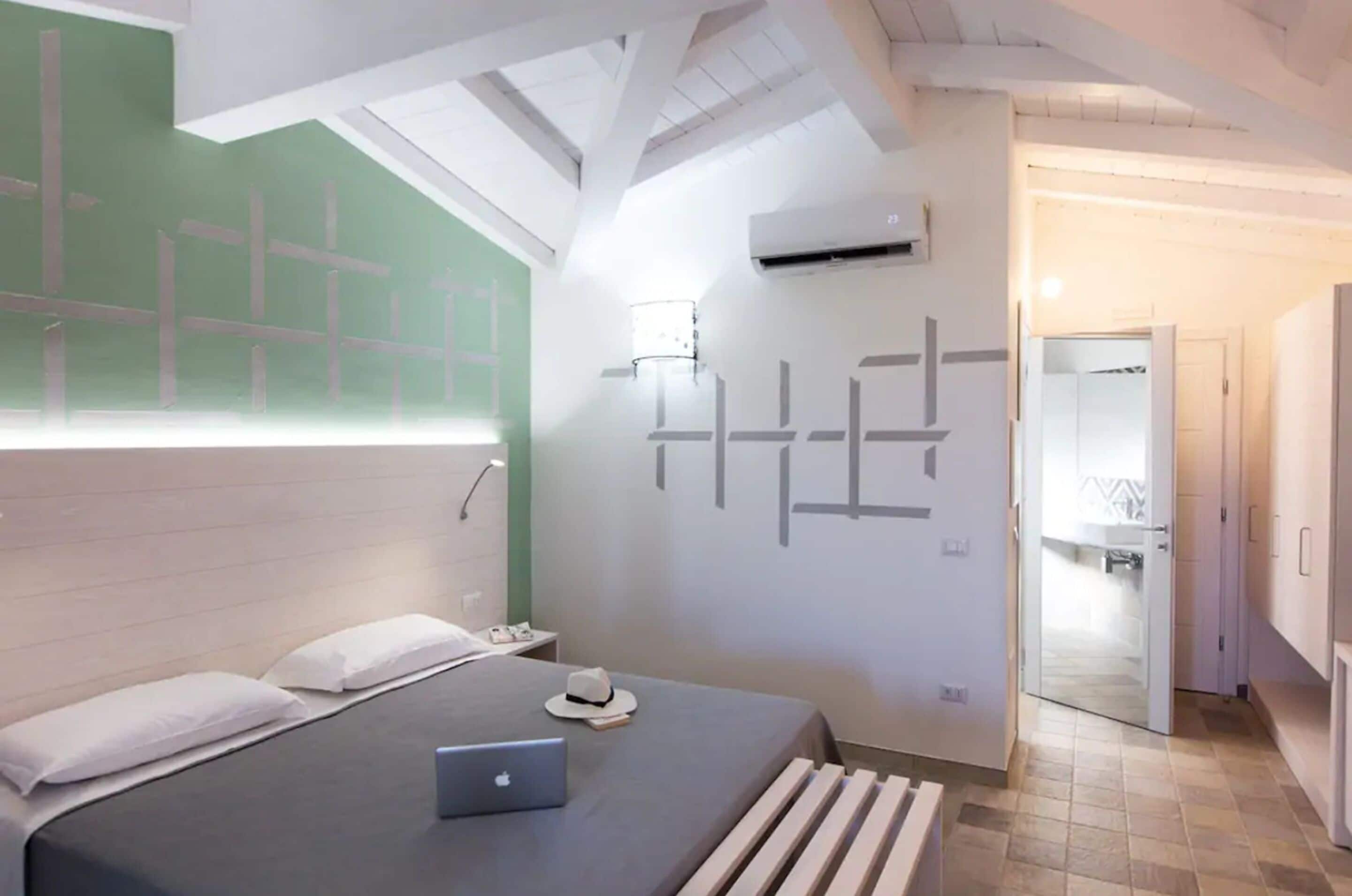 A modern bedroom with a bed, a laptop, and a hat on the bed. There is a window with a view of the outside.