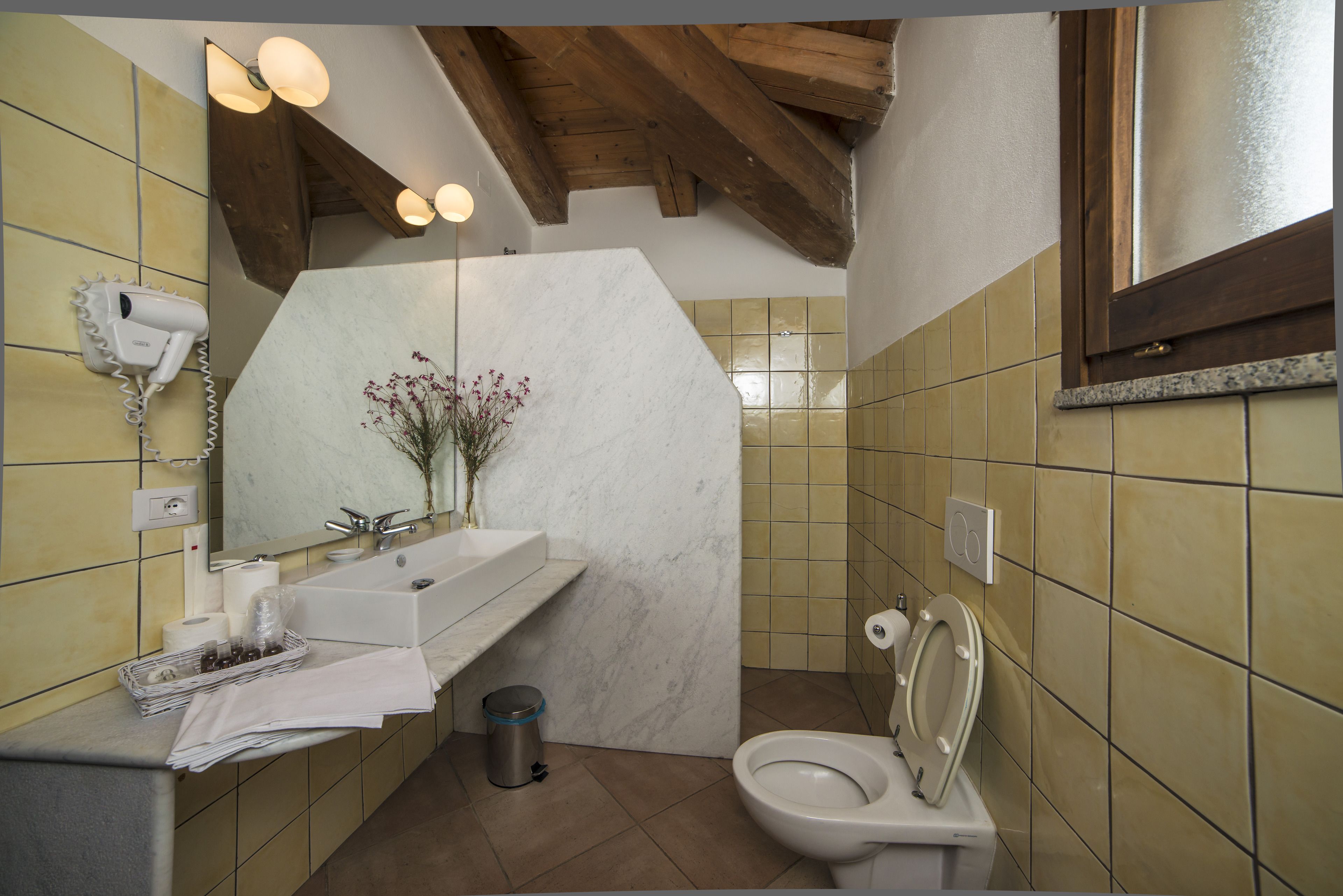 A bathroom with a marble sink, a toilet, and a hairdryer mounted on the wall.