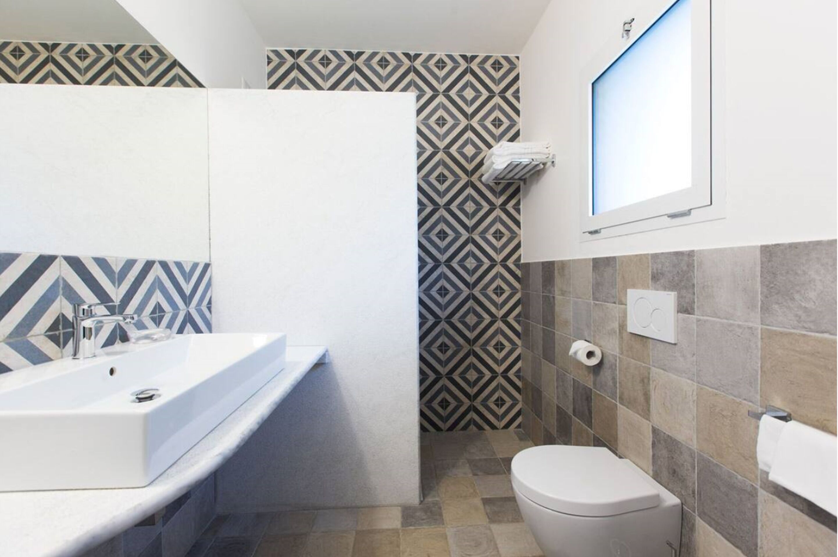 Ein Badezimmer mit einem weißen Waschbecken, einer Toilette und Wandfliesen mit Muster.