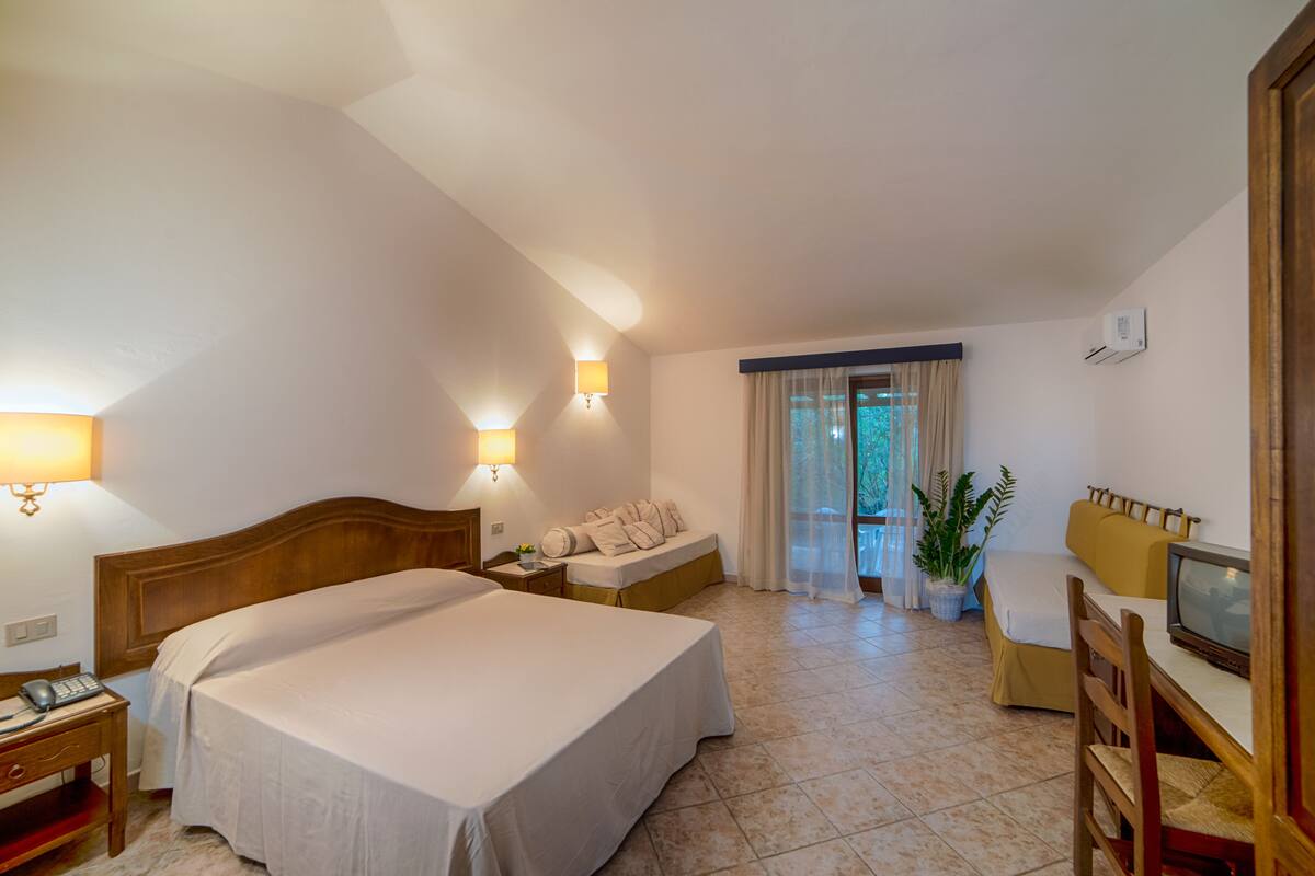 Ein Hotelzimmer mit einem großen Bett, einem Schreibtisch mit Stuhl, einem Fernseher und einer Zimmerpflanze.