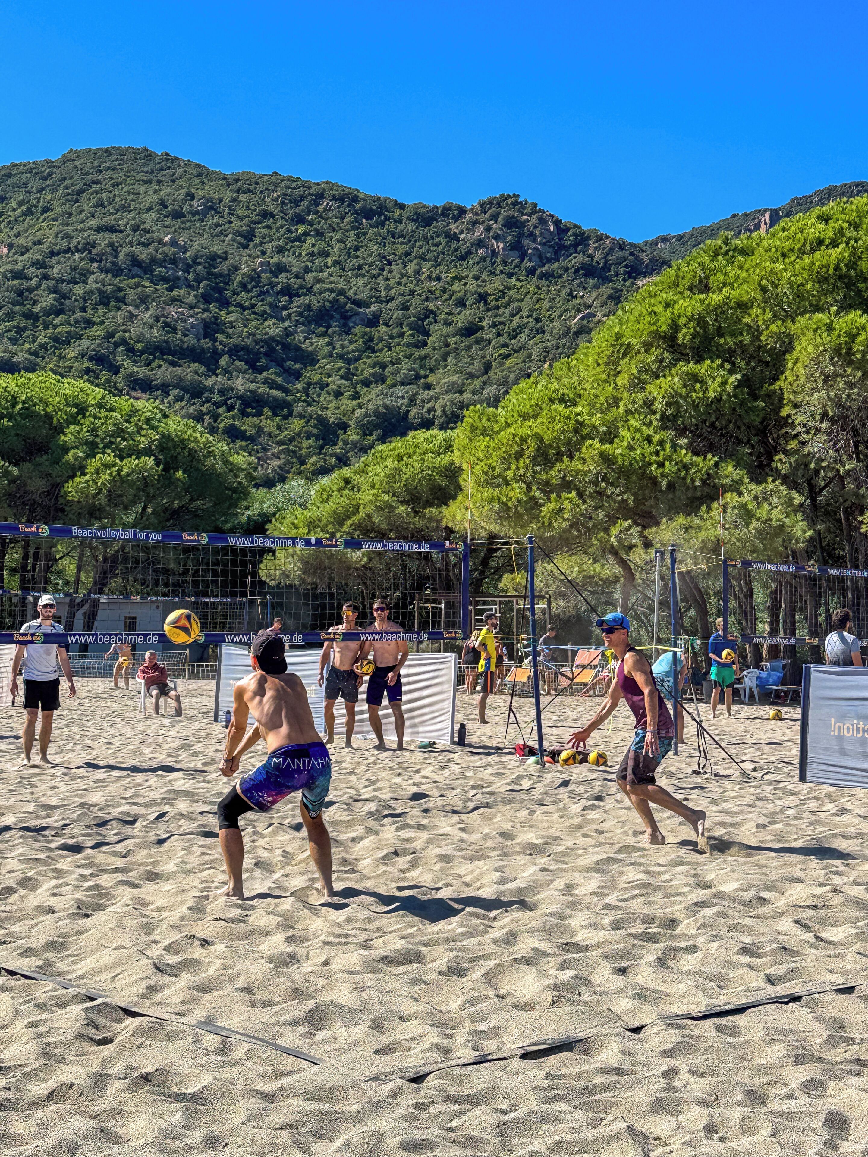 A sandy beach volleyball court with net, surrounded by trees and hills.