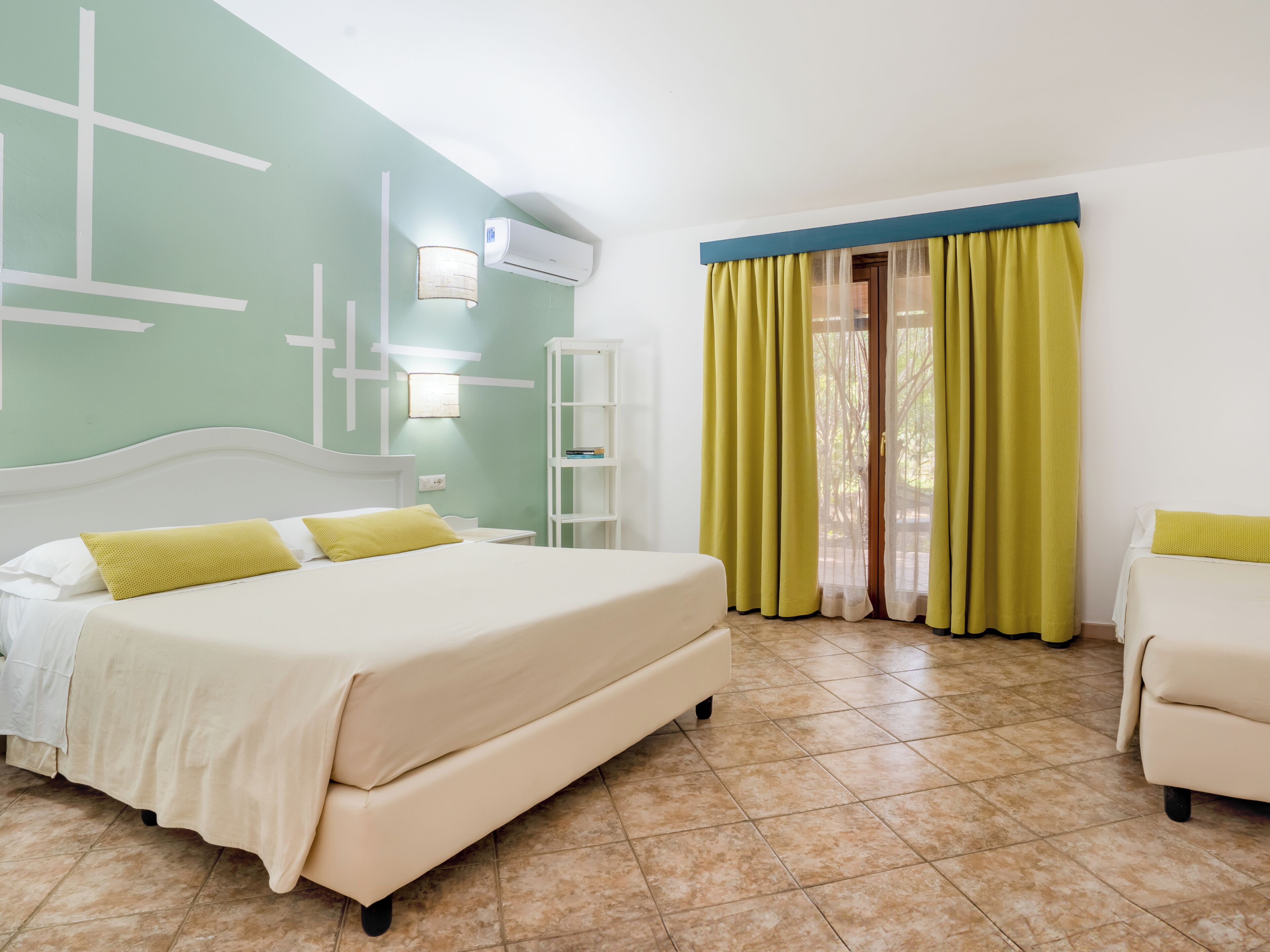 Quarto de hotel com cama, uma cadeira, guarda-roupa e janela com cortinas.