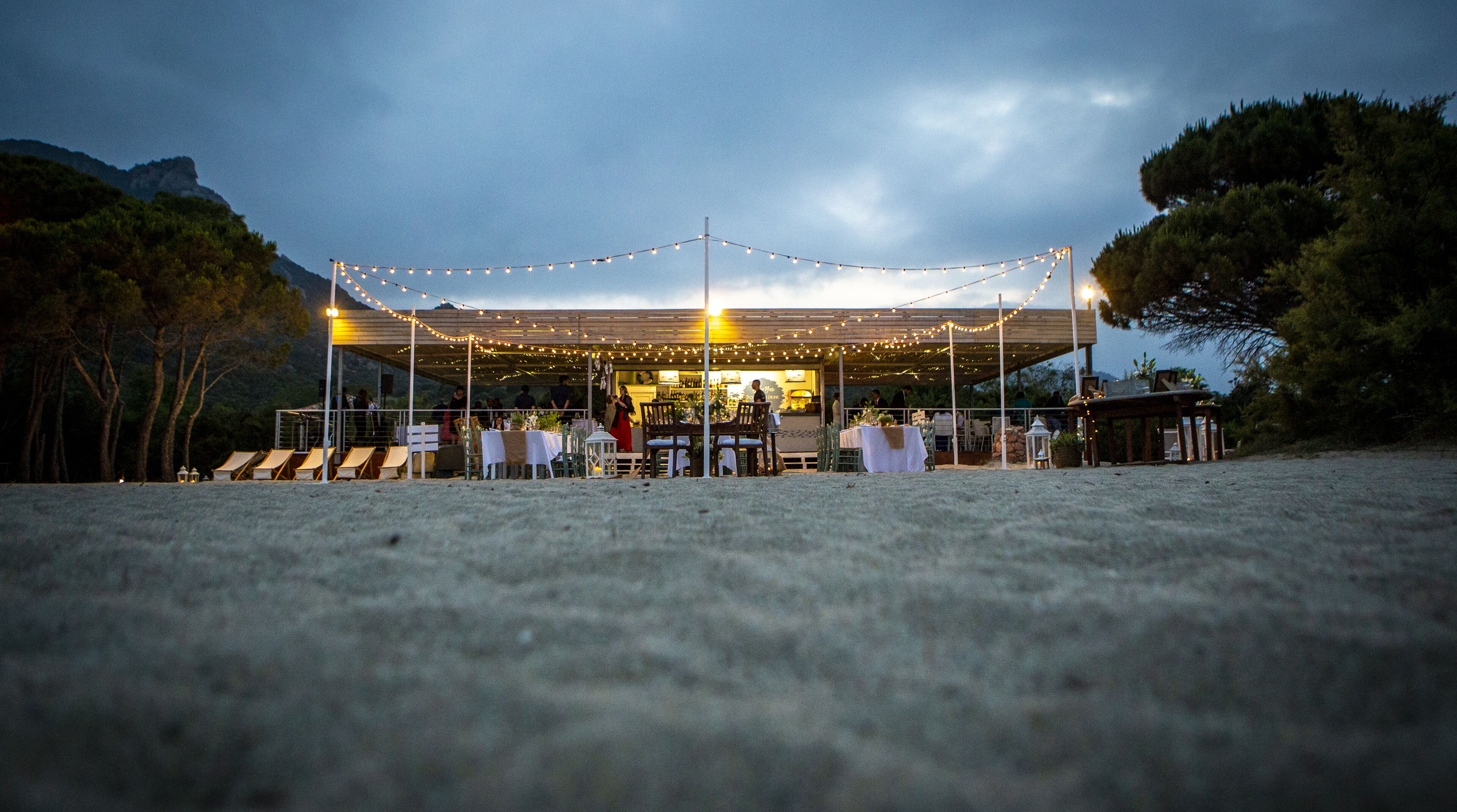Un área de comedor al aire libre con luces colgantes, mesas y sillas.