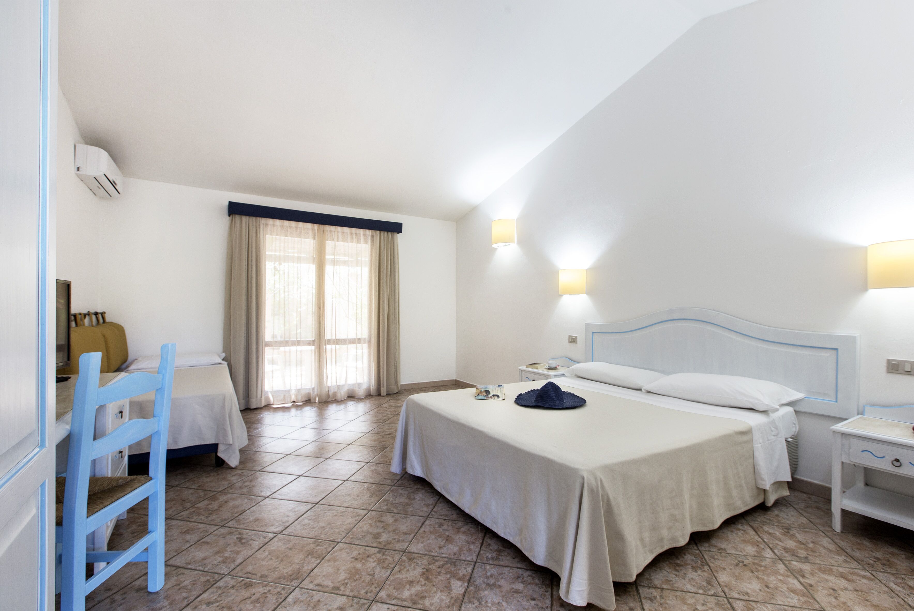 Habitación de hotel con cama, mesitas de noche, escritorio, silla y ventana con cortinas.