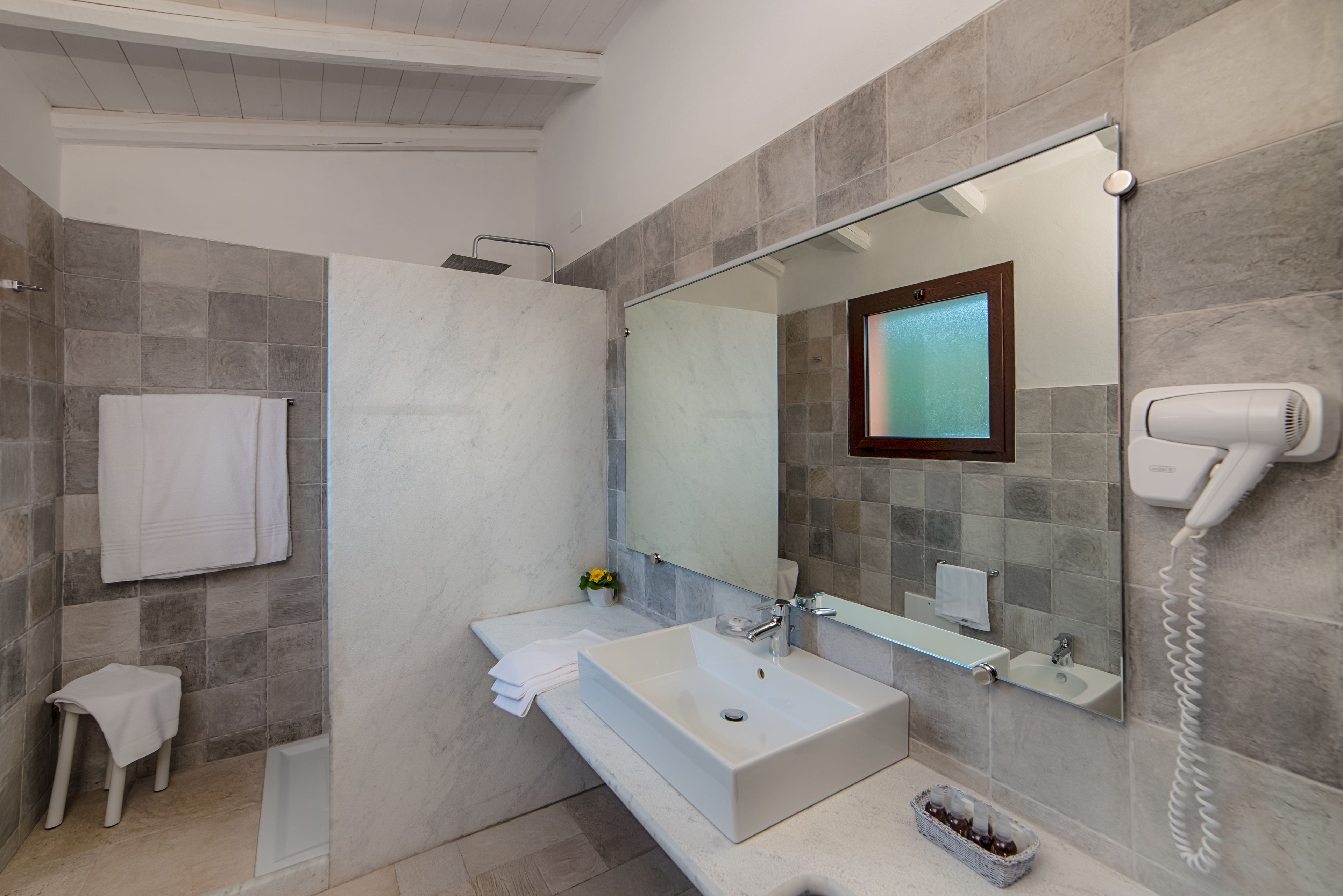 A modern bathroom with a large mirror, a sink, a shower, and a hairdryer.