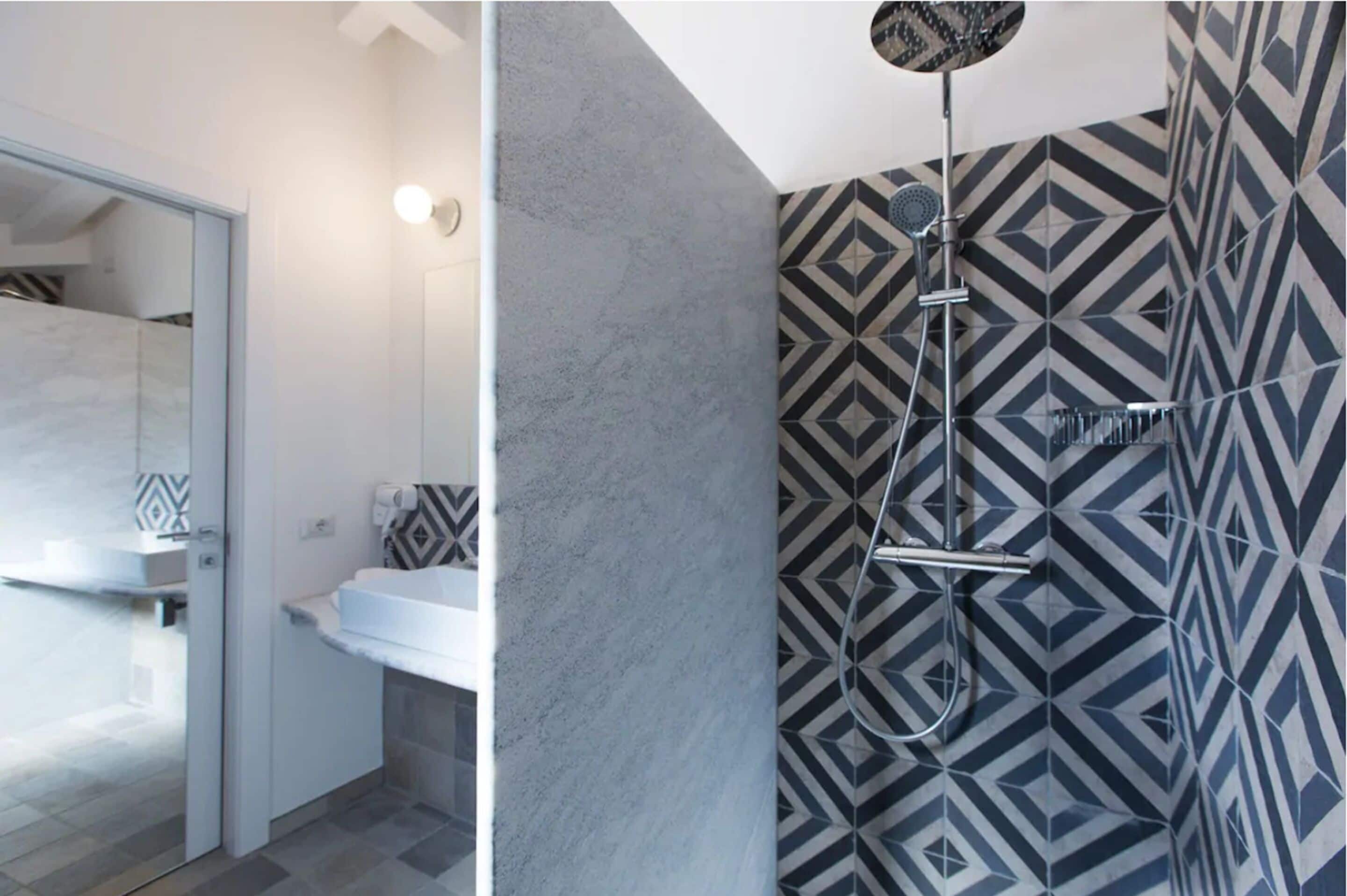 A modern bathroom with a shower, a white sink, and patterned tiles.