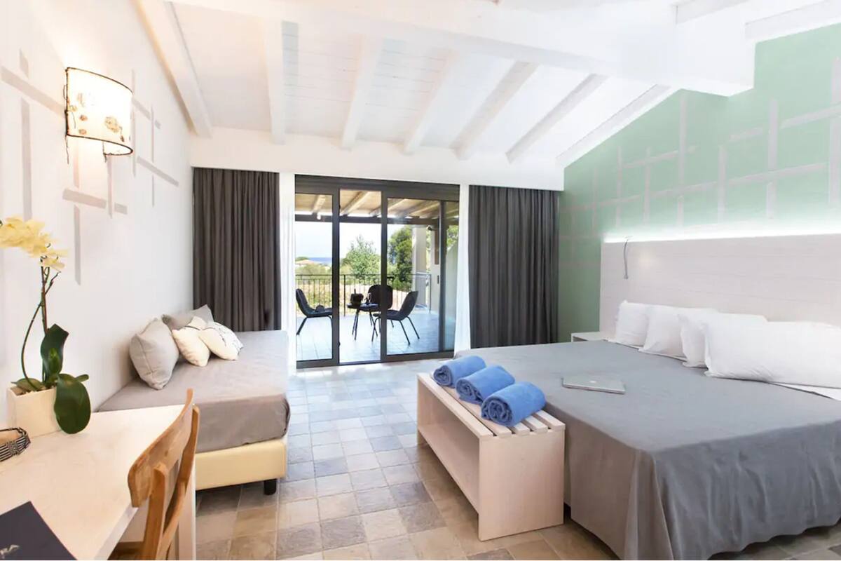 Ein modernes Hotelzimmer mit Bett, Schreibtisch, Stuhl, Bank und Blick ins Freie.