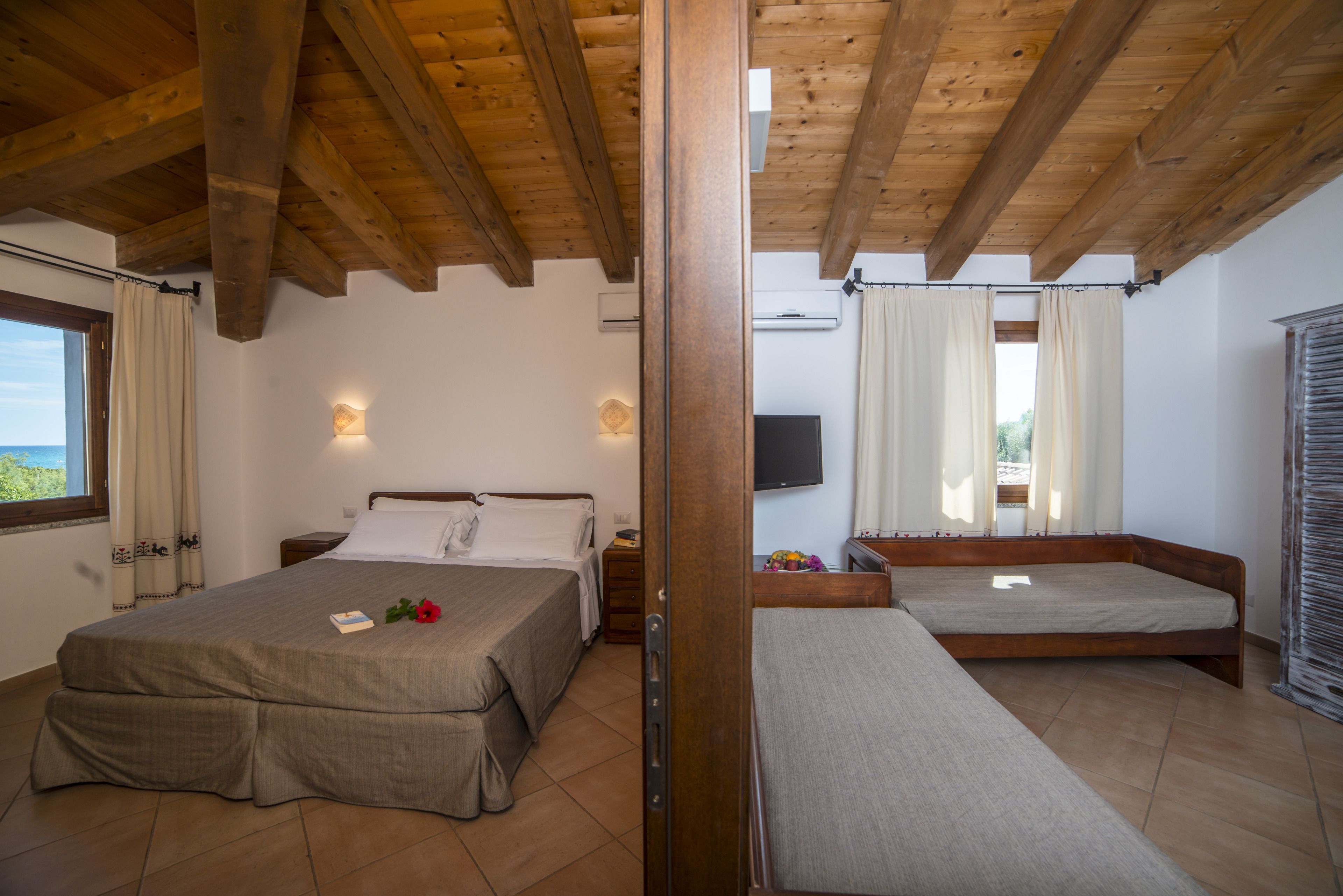 Een slaapkamer met een houten plafond, een bed, een bankje en een televisie.