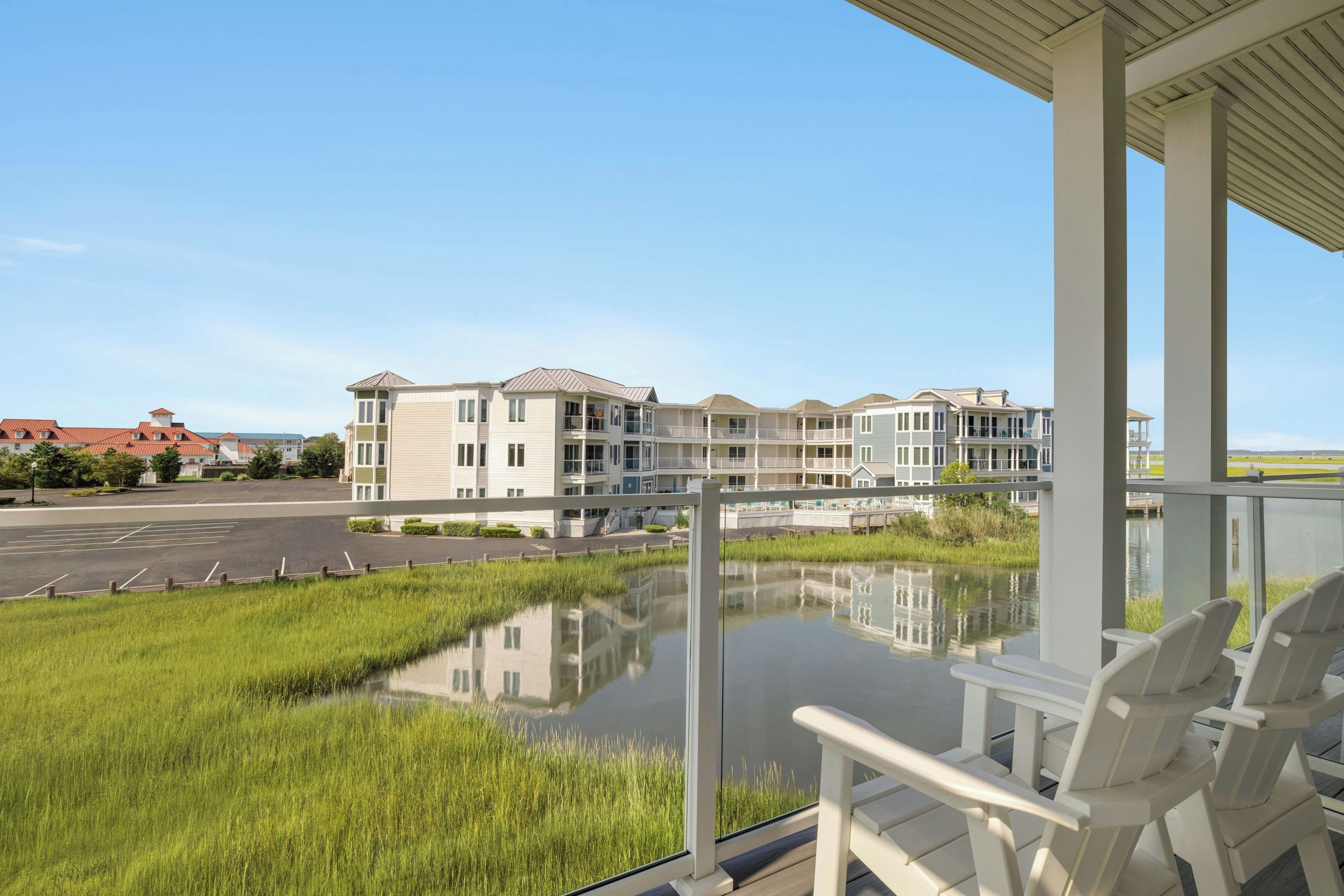 A residential building with multiple balconies, a parking lot, and a body of water in the foreground.
