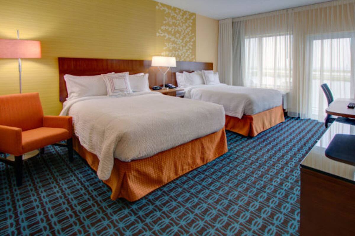 A hotel room with two beds, a desk, a chair, and a patterned carpet.
