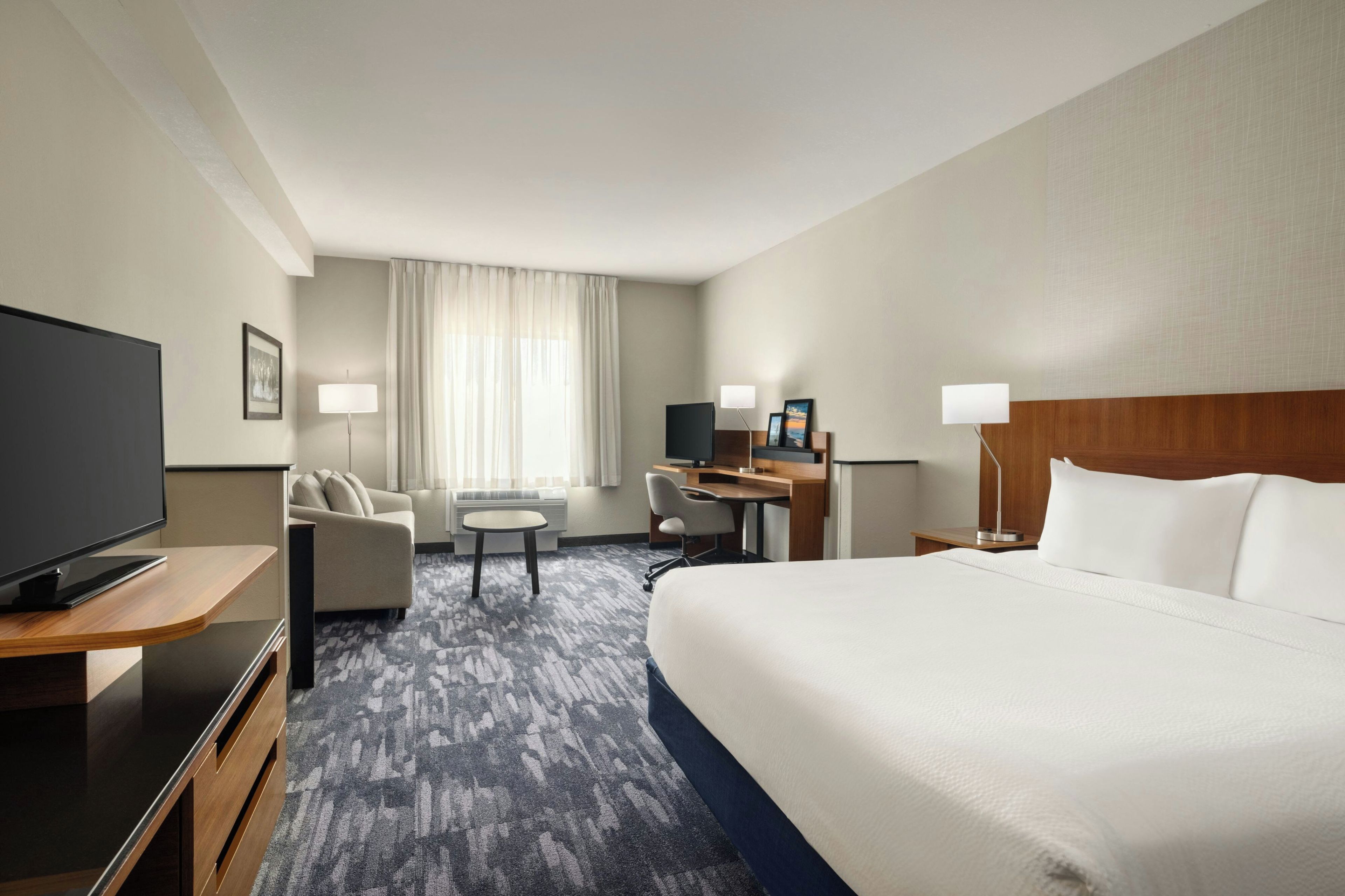 Een hotelkamer met een groot bed, een bureau met een computer, een televisie en een zithoek met een stoel en een bijzettafeltje.