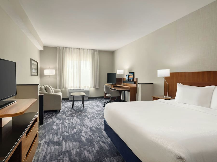 A hotel room with a large bed, a desk with a computer, a TV, and a seating area with a chair and a small table.