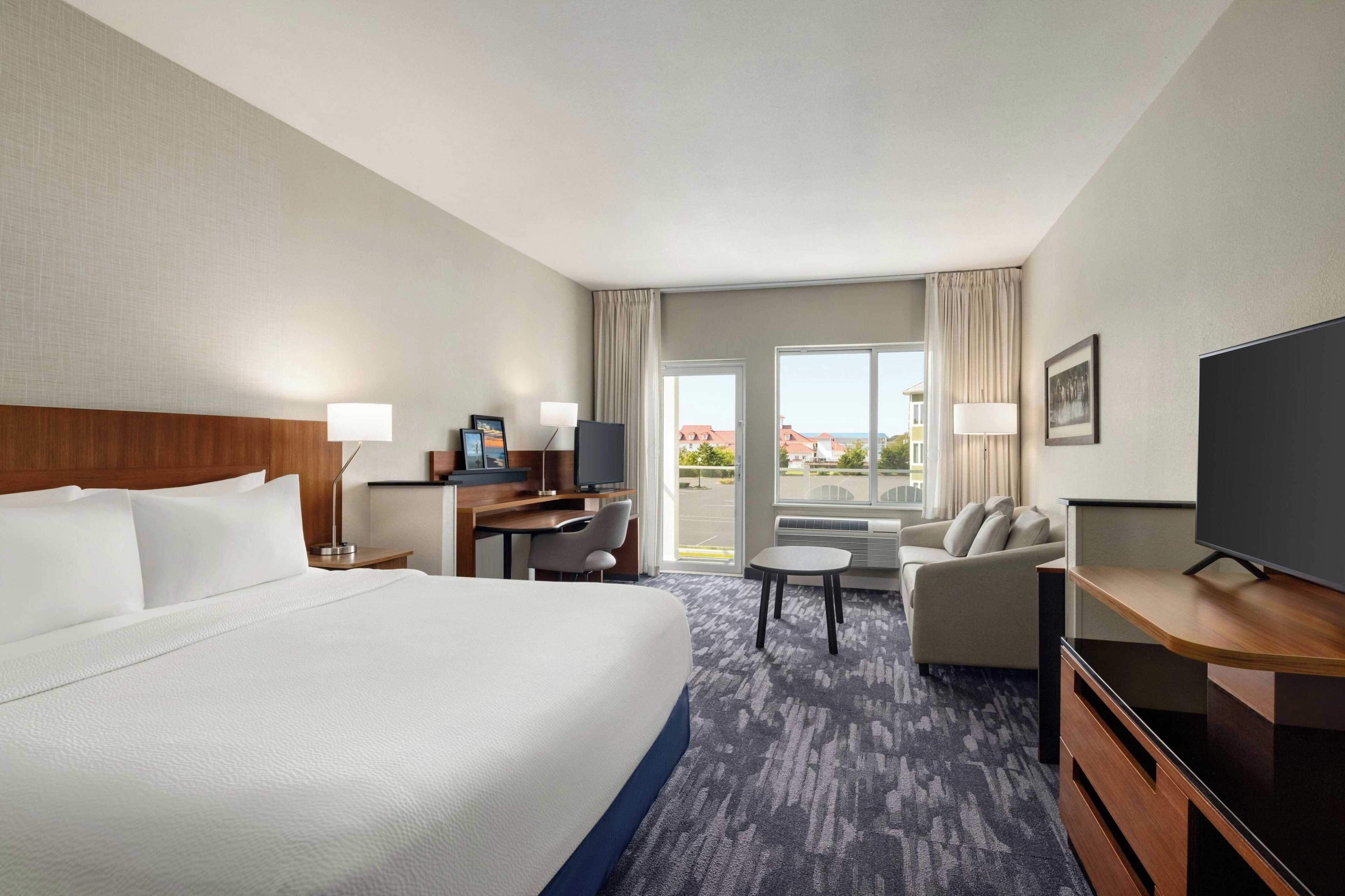Une chambre d’hôtel avec un grand lit, un bureau avec un ordinateur, une télévision, un canapé et une vue sur l’extérieur.