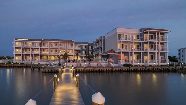 A waterfront hotel with multiple balconies, a dock, and a calm water body.