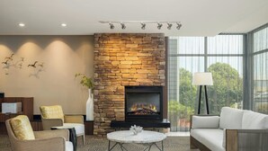 A modern living room with a stone fireplace, comfortable seating, and a large window offering a view of trees.