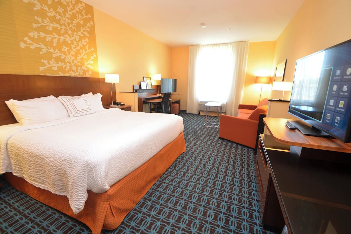 A hotel room with a large bed, a desk with a TV, and a small seating area.