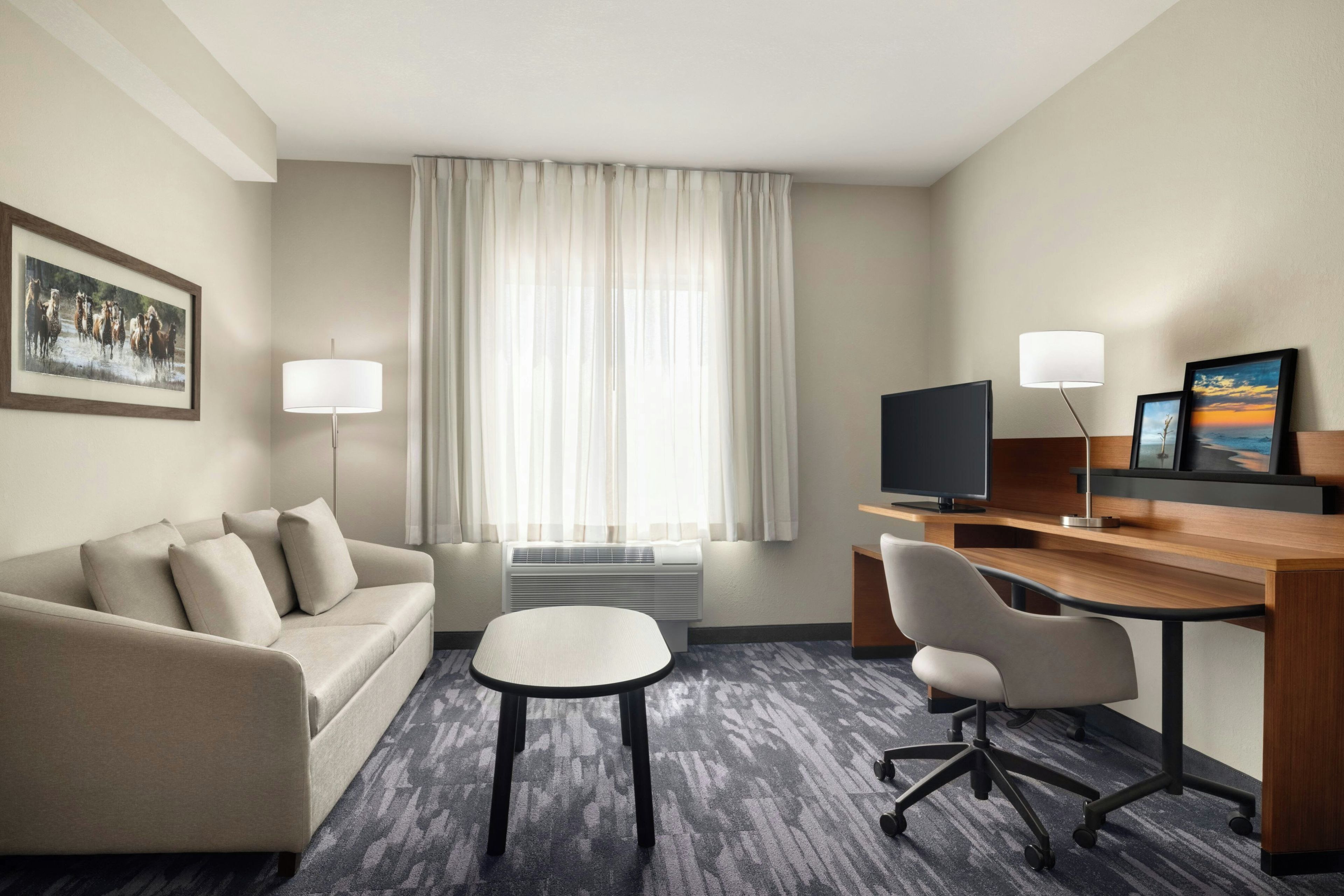 Habitación de hotel con sofá, escritorio con silla, televisión y ventana con cortinas.