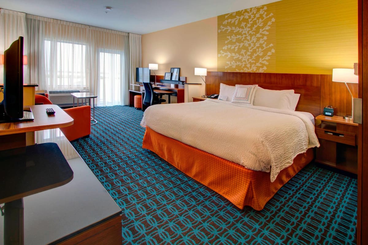 A hotel room with a large bed, a desk with a computer, a chair, and a TV.