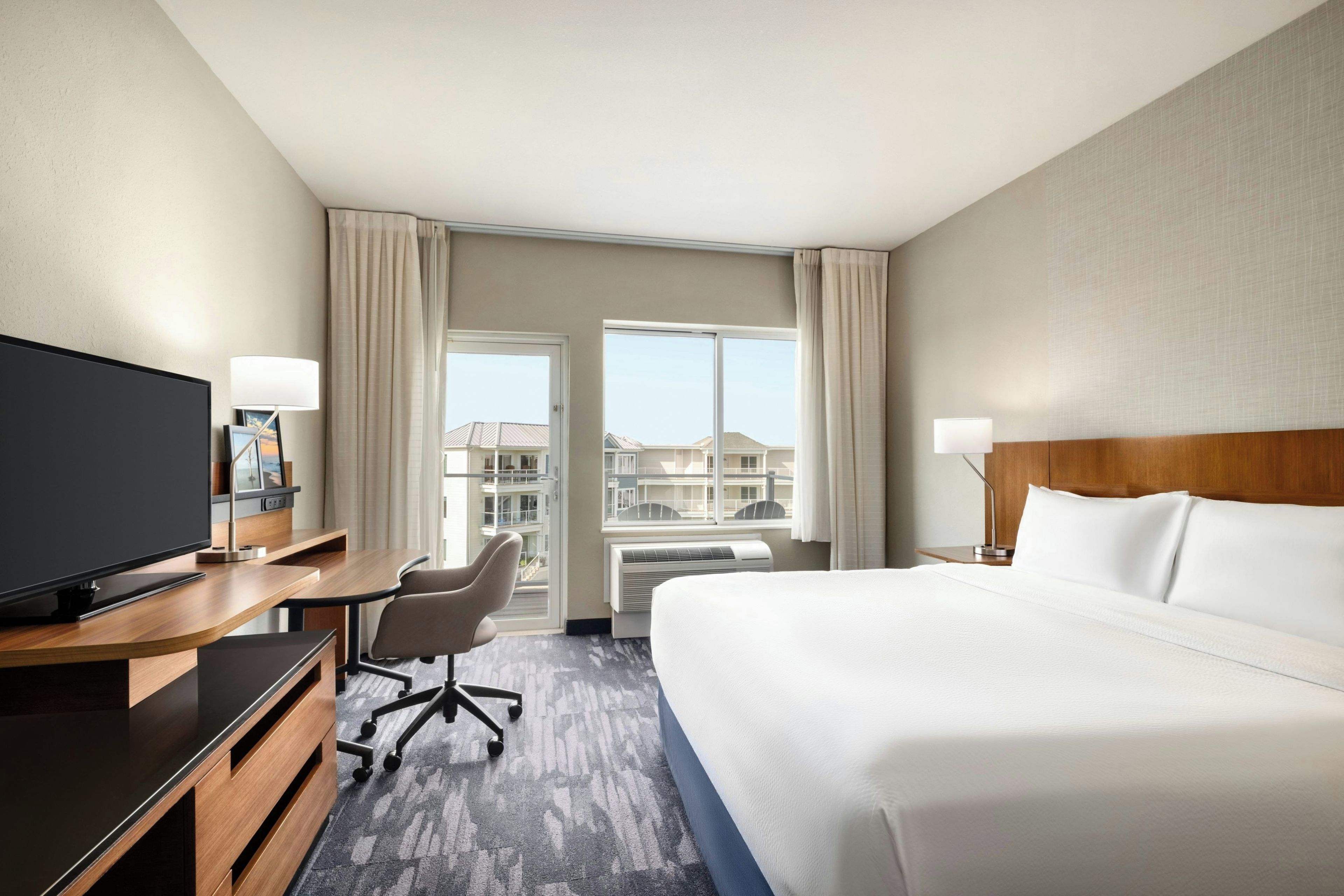 Habitación de hotel con cama, escritorio, silla, televisión y vistas al exterior.