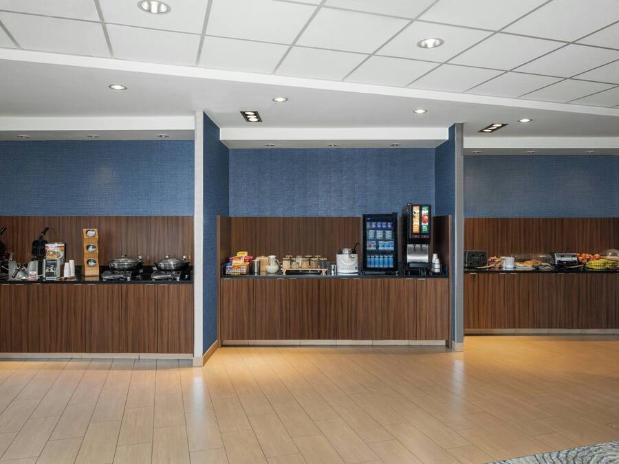 A modern reception area with a wooden counter, a coffee machine, and a refrigerator.