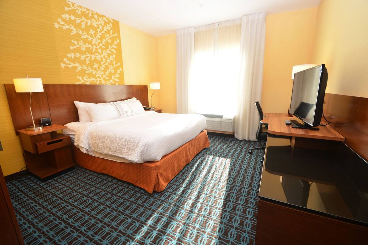 A hotel room with a large bed, bedside lamps, a desk with a computer, and a window with curtains.