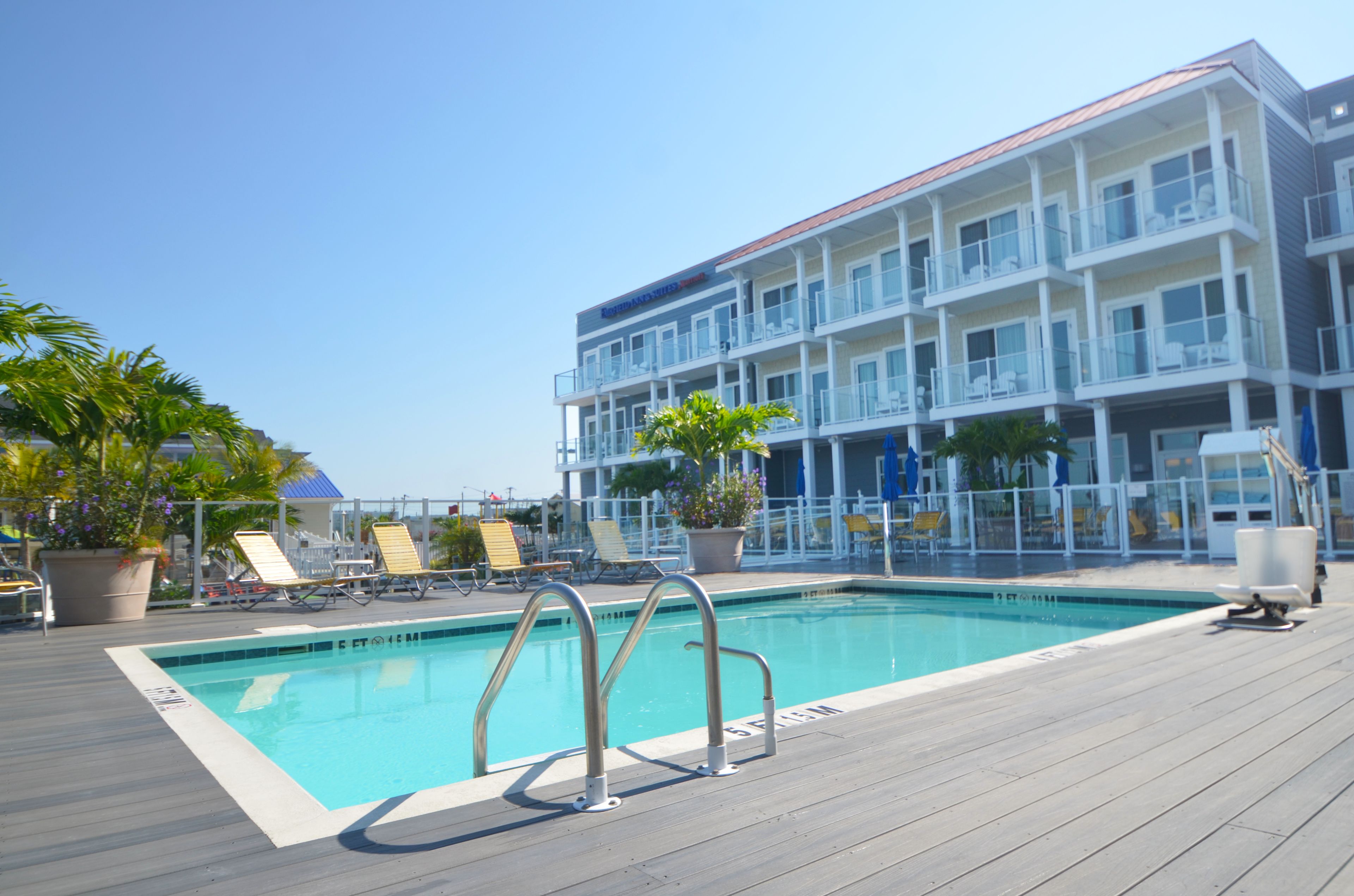 A pool area with lounge chairs and a building with multiple balconies in the background.