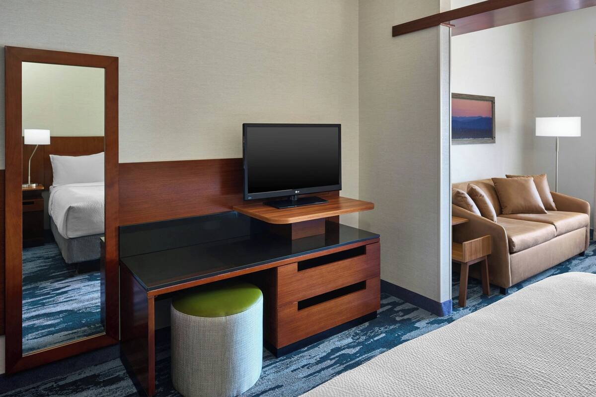 Una camera d'albergo con un letto, una TV su un mobiletto in legno, un divano e uno specchio.