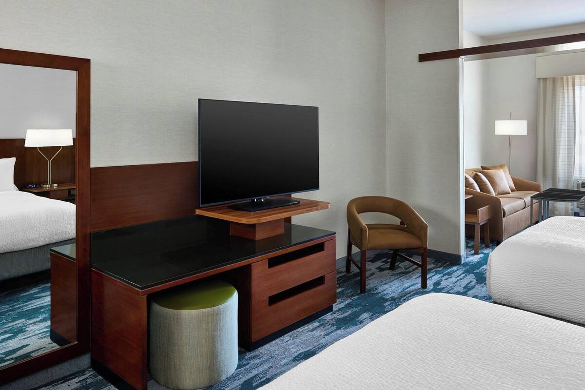 Una camera d'albergo con una TV a schermo piatto su un supporto in legno, una sedia, un letto e uno specchio.