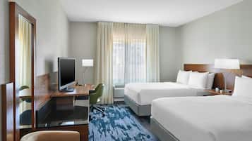 A hotel room with two beds, a desk with a television, a chair, and a large window with curtains.