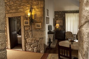 A stone-walled room with a wooden door, a table with a bowl of fruit, and a lamp. - Casa do Ameal (Viana do Castelo)