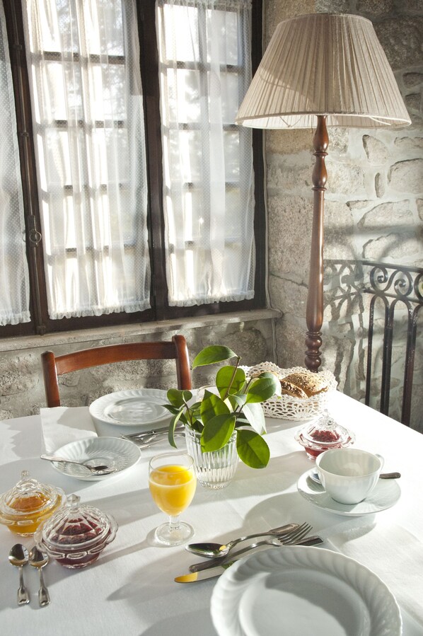 A breakfast table set with plates, cutlery, a glass of orange juice, and a vase with green leaves.