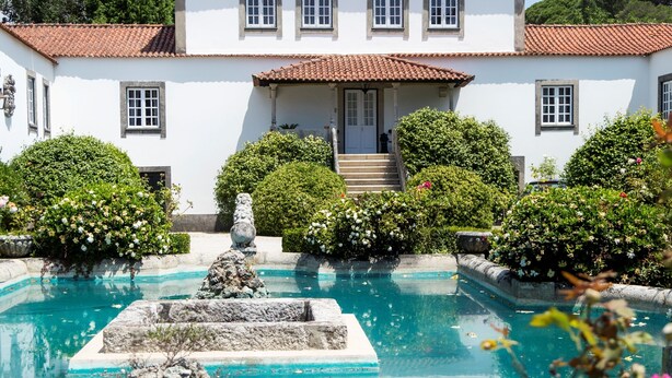 A white building with a tiled roof, a swimming pool with a fountain, and surrounding greenery. - Casa do Ameal (Viana do Castelo)